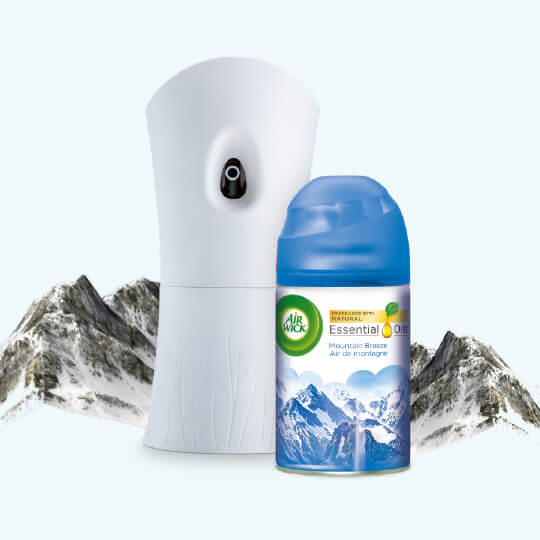 Présente une recharge et un dispositif de vaporisateur automatique Freshmaticᴹᴰ Brise des montagnes parmi des montagnes.