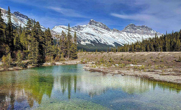 Photo d’un paysage, un lac avec des montagnes et des pins en arrière-plan.